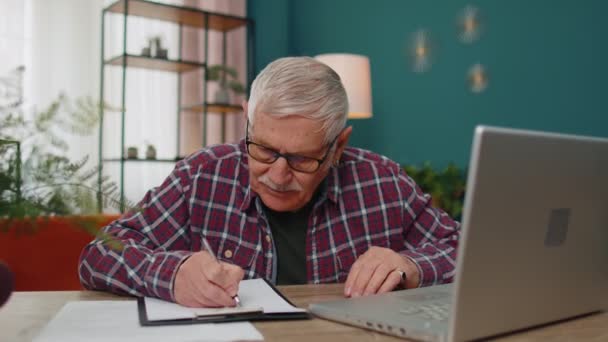 Hombre mayor trabajando en el ordenador portátil, tomando notas en la hoja de papel, molesto por los malos resultados pobres - Imágenes, Vídeo
