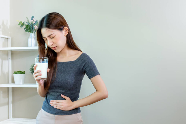 Mujer asiática infeliz sosteniendo leche de vidrio y dolor de estómago después de beber leche. Síntoma de alergia a la lactosa y calcio. - Foto, imagen