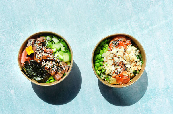 Top view of wok box, bowl of rice on black background. Rice fried and stirred with salmon, avocado, onion, mushrooms, broccoli, sesame. Chinese, Asian food delivery. Packaging for woks.  - Photo, Image
