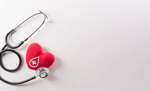 Παγκόσμια ημέρα αιμοδοτών, κόκκινος σταυρός και έννοια ημέρας νοσηλευτών από κόκκινη καρδιά και στηθοσκόπιο σε λευκό φόντο. - Φωτογραφία, εικόνα