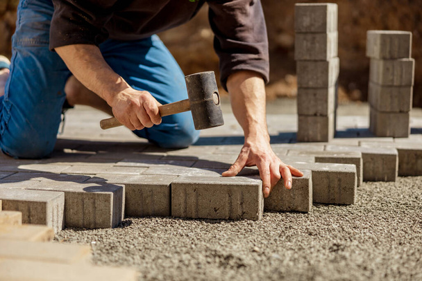 Young man laying gray concrete paving slabs in house courtyard on gravel foundation base. Master lays paving stones. Garden brick pathway paving by professional paver worker. Repairing sidewalk. - Foto, Imagen
