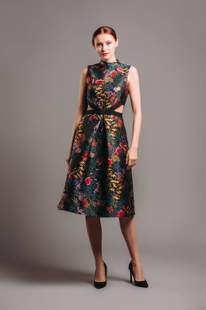 Cut out waist midi dress in floral embroidery with black high heels. Ginger lady posing in studio. Evening colourful elegant gown with high neck line, female fashion, gorgeous chic look. - Photo, Image
