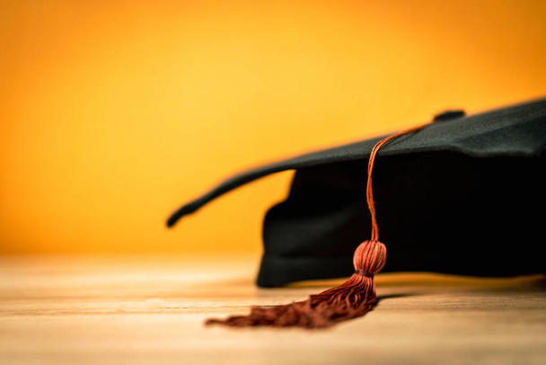 Μαύρο καπέλο αποφοίτησης τοποθετείται σε ξύλινο γραφείο φόντο - Φωτογραφία, εικόνα