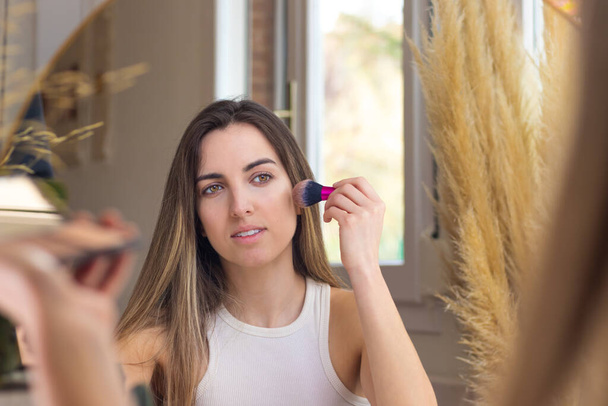 Woman looking at the mirror while contouring her face in the make up process - Foto, Bild