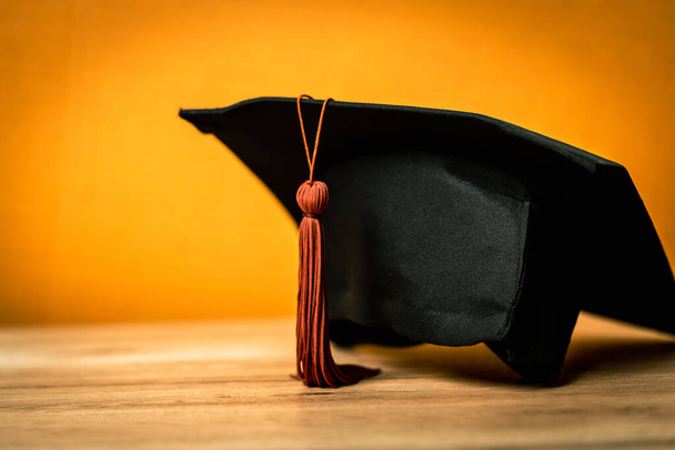 Μαύρο καπέλο αποφοίτησης τοποθετείται σε ξύλινο γραφείο φόντο - Φωτογραφία, εικόνα