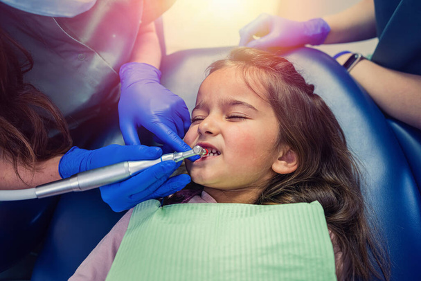 молода кваліфікована жінка-стоматолог чистить зуби маленькій дитині, яку доставили на прийом. Концепція чищення молочних зубів
 - Фото, зображення