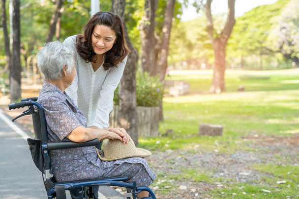 Gondozó segítséget és ellátást ázsiai idős vagy idős hölgy beteg ül és boldog a kerekesszékben a parkban, egészséges erős orvosi koncepció. - Fotó, kép