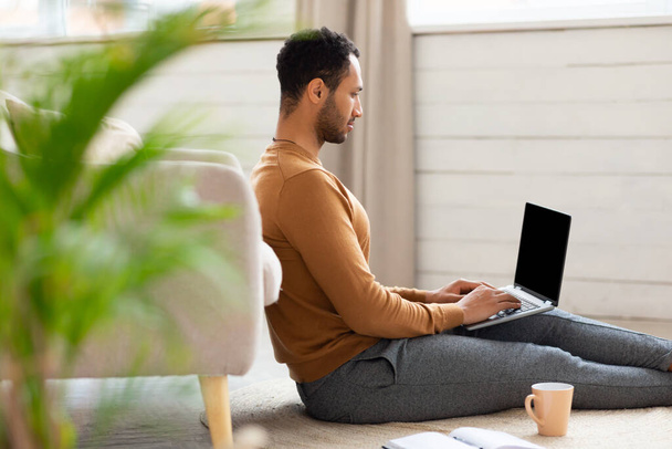 Arab férfi használ laptop ül a padlón otthon - Fotó, kép