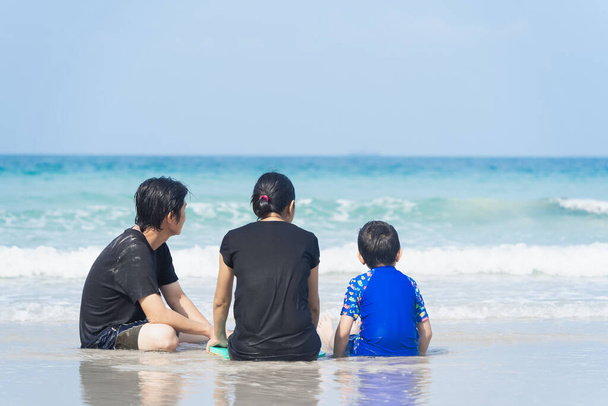 Famille asiatique assis sur la plage en regardant la mer bleue, l'île, la lumière du soleil et le ciel bleu le matin. - Photo, image