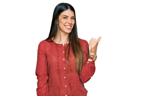 Young hispanic woman wearing casual clothes smiling with happy face looking and pointing to the side with thumb up.  - Foto, Imagen