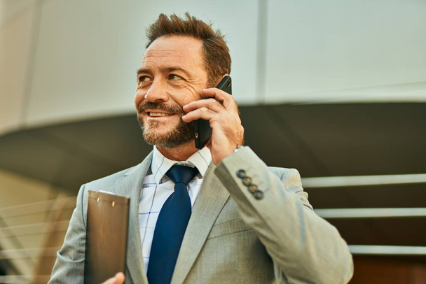 Бізнесмен середнього віку посміхається щасливий виступ на смартфоні в місті
. - Фото, зображення