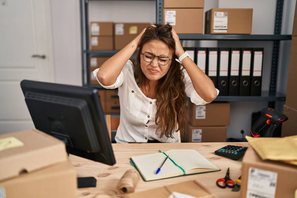 Young hispanic woman working at small business ecommerce suffering from headache desperate and stressed because pain and migraine. hands on head.  - Fotoğraf, Görsel