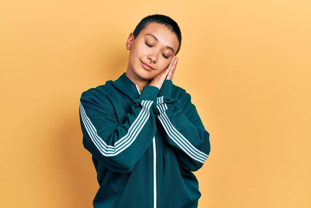 Beautiful hispanic woman with short hair wearing sporty jacket sleeping tired dreaming and posing with hands together while smiling with closed eyes.  - Фото, изображение