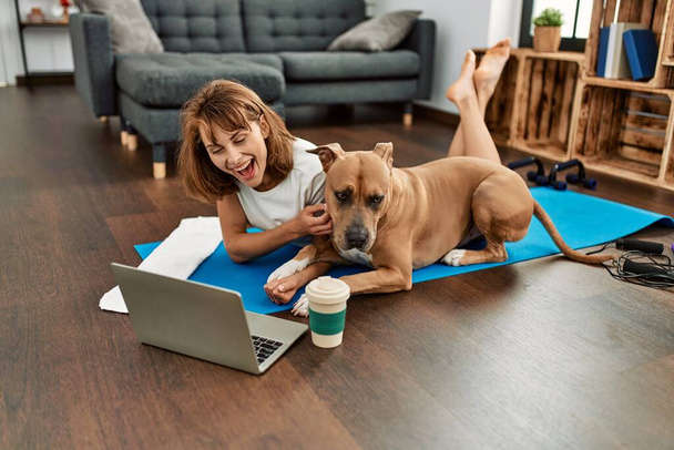 młody biały kobieta sportswoman uśmiechnięty pewny za pomocą laptop z pies w domu - Zdjęcie, obraz