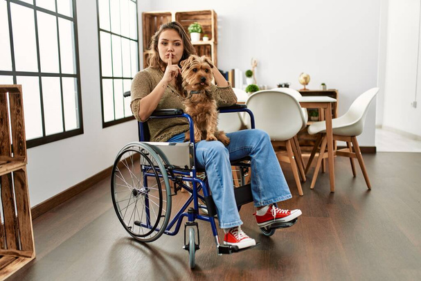 Молодая латиноамериканка, сидящая дома на инвалидной коляске, указывает пальцем в камеру со счастливым и смешным лицом. хорошая энергия и вибрации.  - Фото, изображение
