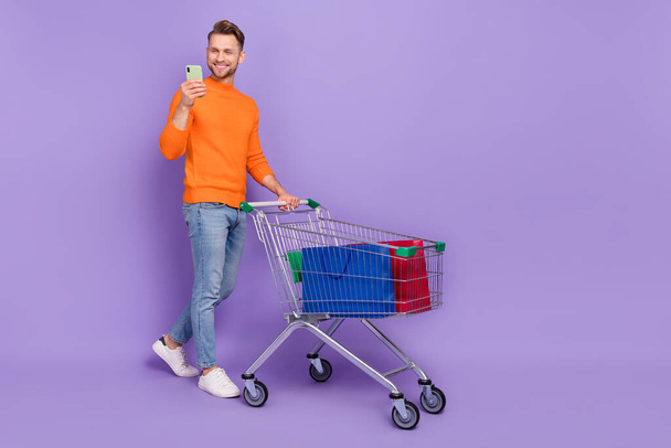 Foto completa de la emoción positiva hombre ir de compras charlando con amigos en el teléfono aislado en el fondo de color violeta - Foto, imagen