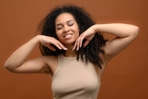 Delightfully charming and attractive young african woman with eyes closed over brown background - Foto, afbeelding