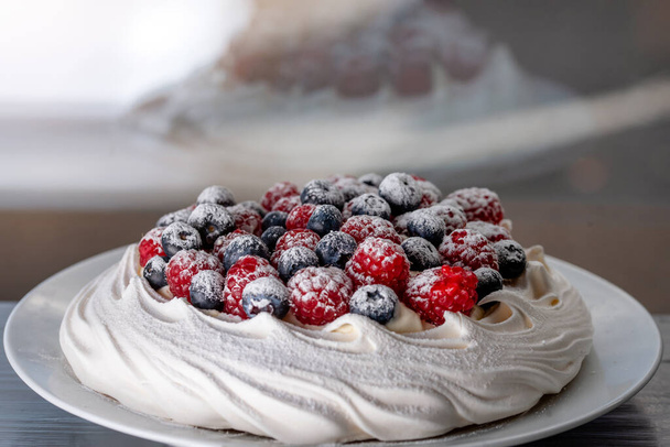 meringue cake with blueberries and raspberries on a plate on green background - Photo, image