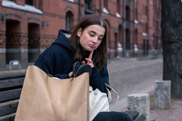 Nuori nainen istuu penkillä käsilaukku ja paketti, käsite ostoksia, kaupungin kävellä. - Valokuva, kuva