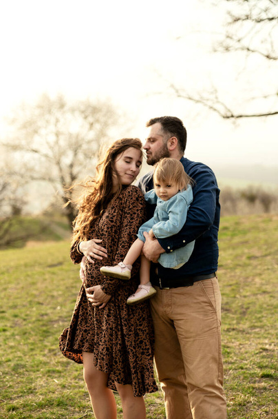 uma família jovem e feliz caminha na natureza com sua filha. mulher grávida em um passeio com sua família. passeio de primavera - Foto, Imagem