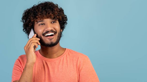 Closeup of positive indian guy having phone conversation on blue - Foto, Bild