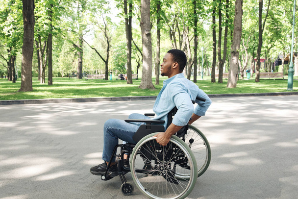 Vista lateral del joven negro en silla de ruedas pasando tiempo en el parque de la ciudad, longitud completa - Foto, imagen