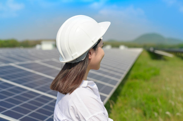 A female engineer wearing helmet in Photovoltaic Cell Farm or Solar Panels Field, eco friendly and clean energy. - Foto, afbeelding