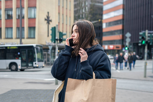 Młoda kobieta w mieście rozmawia przez telefon z paczką w rękach, koncepcja zakupów, spacer po mieście. - Zdjęcie, obraz