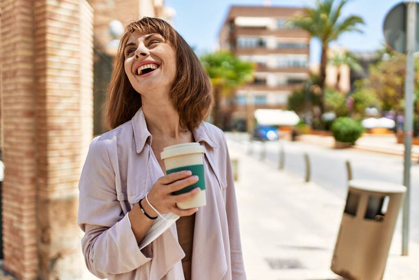 Giovane ragazza caucasica sorridente felice bere caffè in città. - Foto, immagini