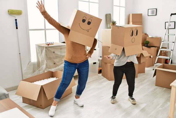 Зрелая мать и синдром Дауна дочь переезжает в новый дом, стоя в картонных коробках со смешными лицами над головой - Фото, изображение