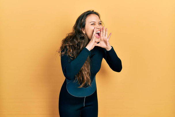 Genç İspanyol kız dalgıç neoprene üniforması giyiyor ve elleri ağzında bağırıyor.  - Fotoğraf, Görsel
