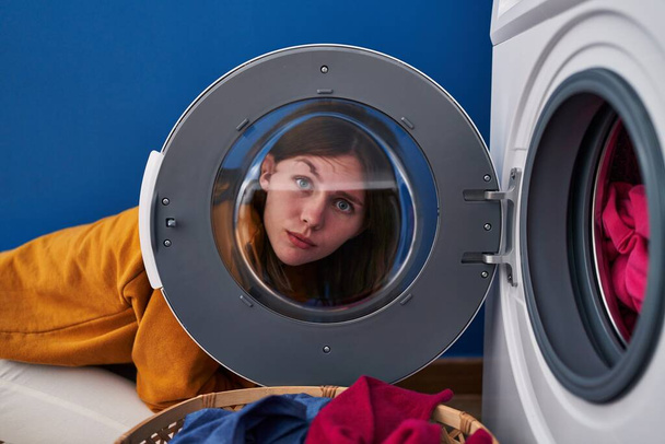Giovane donna bruna che guarda attraverso la finestra della lavatrice scettica e nervosa, accigliata sconvolta a causa di un problema. persona negativa.  - Foto, immagini