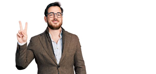 Junger hispanischer Mann mit Businessjacke und Brille zeigt mit Fingern Nummer zwei nach oben und lächelt dabei selbstbewusst und glücklich.  - Foto, Bild