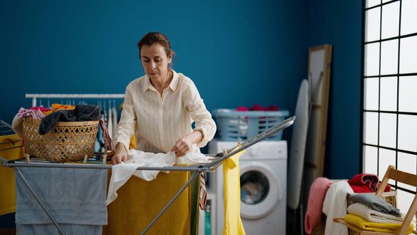Middle age hispanic woman hanging clothes on clothesline at laundry room - Photo, image