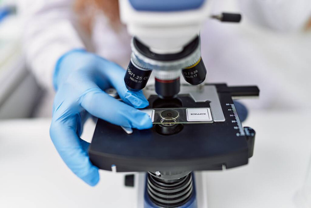 Jeune homme rousse portant un uniforme de scientifique au microscope au laboratoire - Photo, image