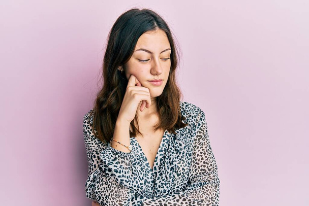 Young brunette woman wearing elegant animal print shirt thinking concentrated about doubt with finger on chin and looking up wondering  - Foto, Bild