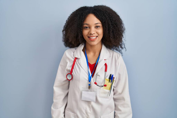 Młoda Afroamerykanka ubrana w mundur lekarza i stetoskop mruga wzrokiem przed kamerą z seksowną ekspresją, radosną i szczęśliwą twarzą.  - Zdjęcie, obraz