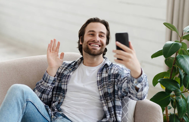 Feliz millennial europeo hombre con rastrojos en el chat casual por vídeo en línea, saludando de la mano a la cámara - Foto, imagen