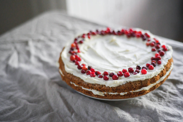 Um delicioso bolo de cenoura está sobre a mesa, decorado com creme de mascarpone branco e cranberries. Uma bela sobremesa para todos os dias - Foto, Imagem