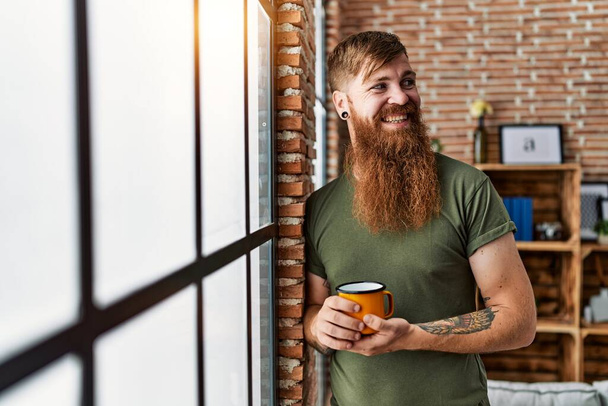 Молодий рудий чоловік посміхається впевнено п'є каву вдома
 - Фото, зображення