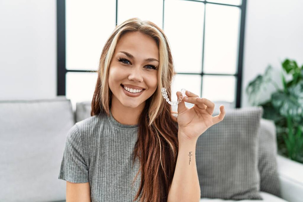 Young caucasian woman holding invisible aligner orthodontic looking positive and happy standing and smiling with a confident smile showing teeth  - Foto, Imagen