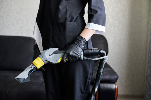 Close up of female housekeeper arm cleaning sofa with washing vacuum cleaner . Cleaning service company employee removing dirt from furniture in flat with professional equipment - Fotó, kép