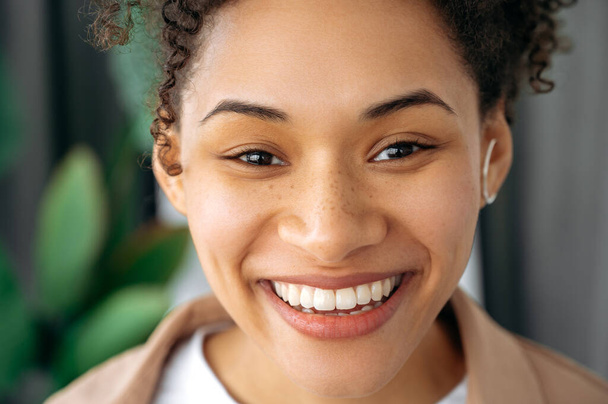 Знімок красивої афроамериканської дівчини з кучерявим волоссям, змішаної раси з веснянками, дивлячись на камеру, усміхаючись, показуючи свою білу сніжно-білу посмішку. - Фото, зображення