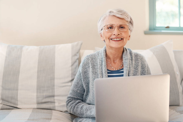 By far the easiest way to stay current. Shot of a senior woman using a laptop on the sofa at home. - Фото, изображение