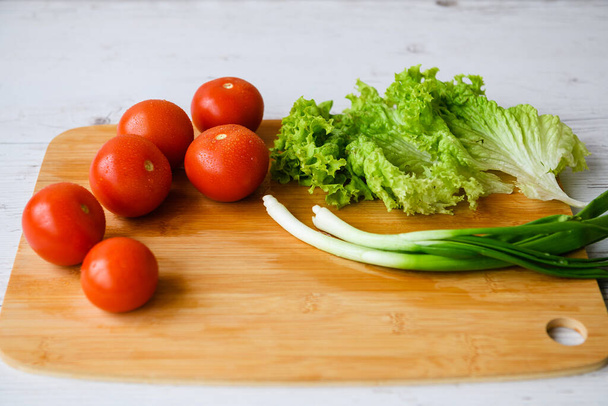 Las verduras frescas para la ensalada se acuestan sobre la mesa de madera con la tabla de cortar. Primer plano. - Foto, Imagen
