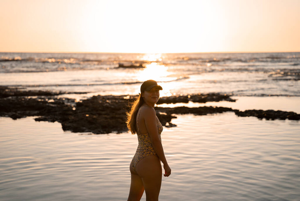 Nuori blondi nainen poseeraa onnellisesti wwearing lippis rannalla kesän auringonlaskun aikana - Valokuva, kuva