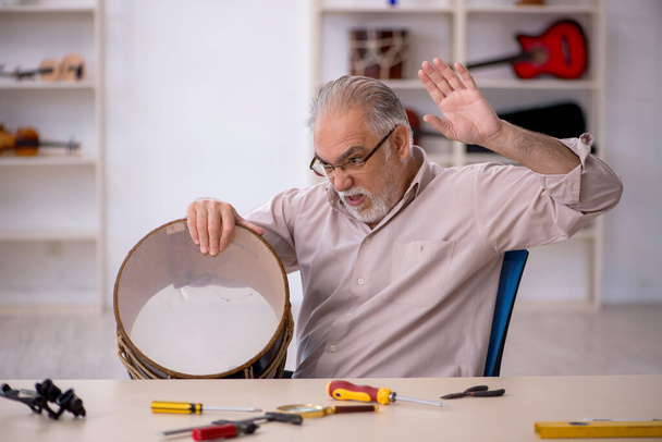 Starý opravář mužského pohlaví opravuje hudební nástroje v dílně - Fotografie, Obrázek
