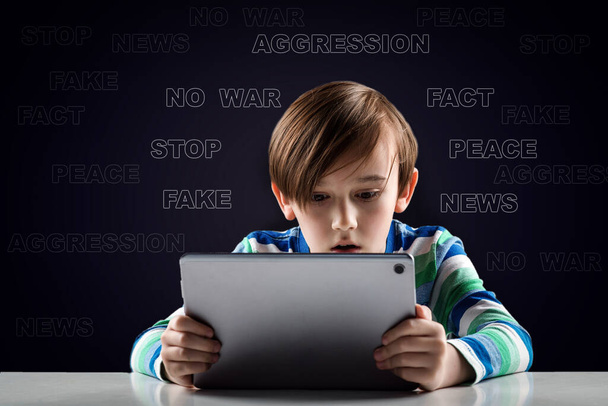 A cute child watches military news in the basement against the background of a wall with inscriptions. Breaking News about the war. Fake or true, who to believe. - Photo, Image