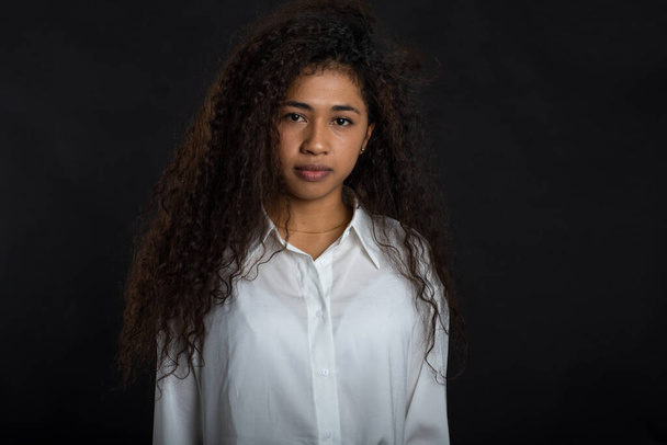 Serious young woman in white shirt looking at camera on black background - Foto, imagen