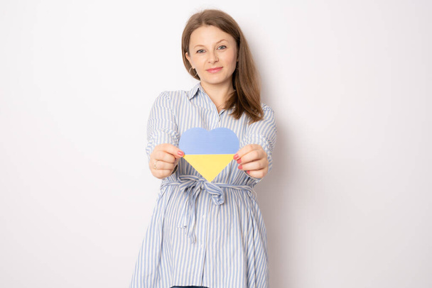 Young smiling pregnant woman showing ukraine paper heart standing isolated over white background. - Photo, Image